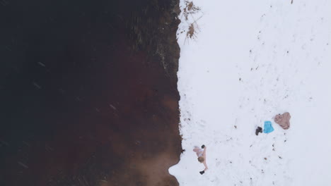 Wide-aerial-plan-view-of-a-woman-entering-icy-lakewater-for-her-routine-plunge