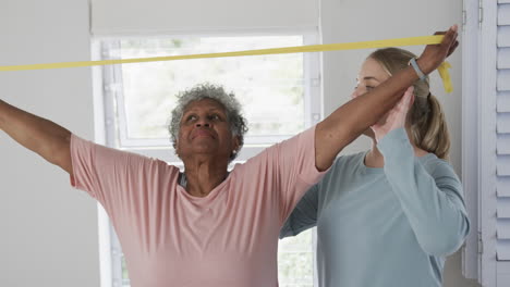 Caucasian-nurse-with-senior-woman-exercising-with-rubber-band,-copy-space,-slow-motion