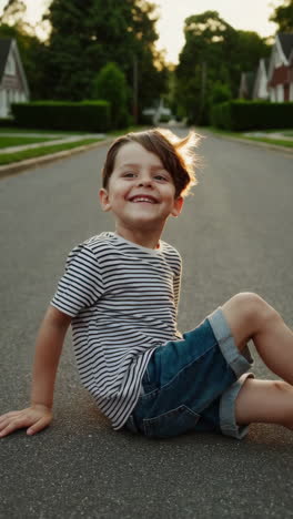 joyful young boy sitting on a residential street in warm sunlight