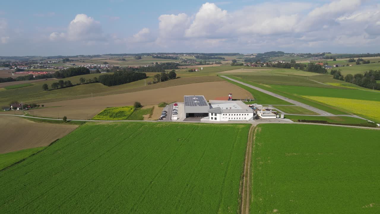 Industriel produktionsanlæg med solpaneler på taget beliggende i åbent landbrugslandskab, der viser bæredygtig energiinfrastruktur og et landligt produktionssted.