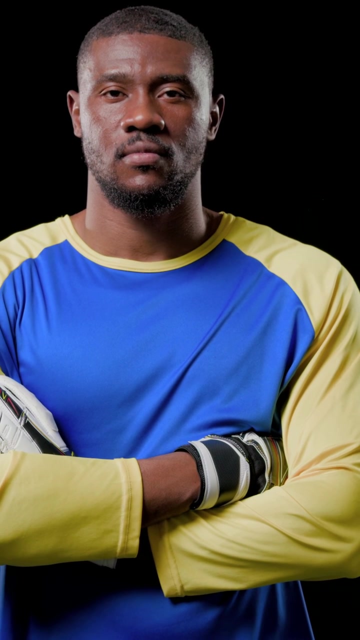 Vídeo vertical: Câmera se afastando de goleiro segurando a bola com camisa e luvas azul-amarelas para retrato.