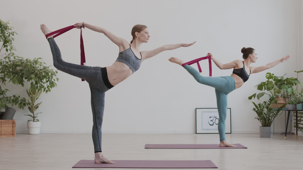 dos mujeres jóvenes usando cinturones de yoga durante la clase de yoga