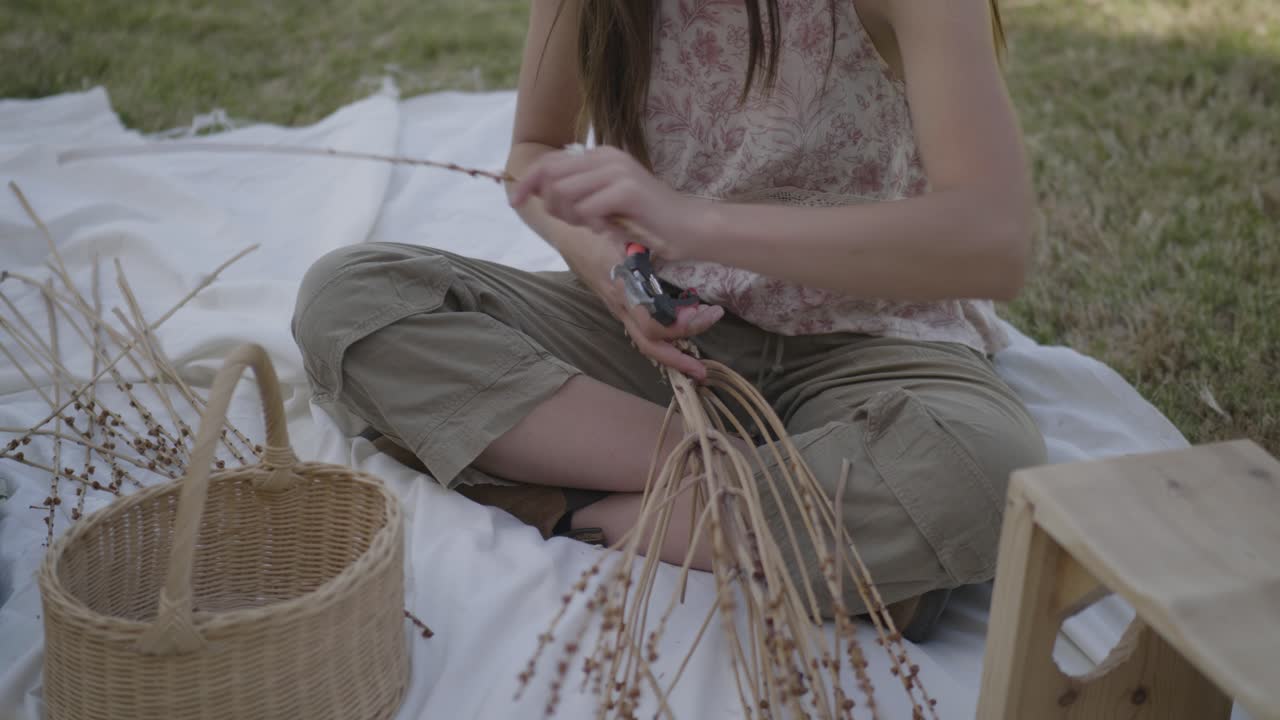 young woman creating a natural craft with dried twigs on a blanket outdoors