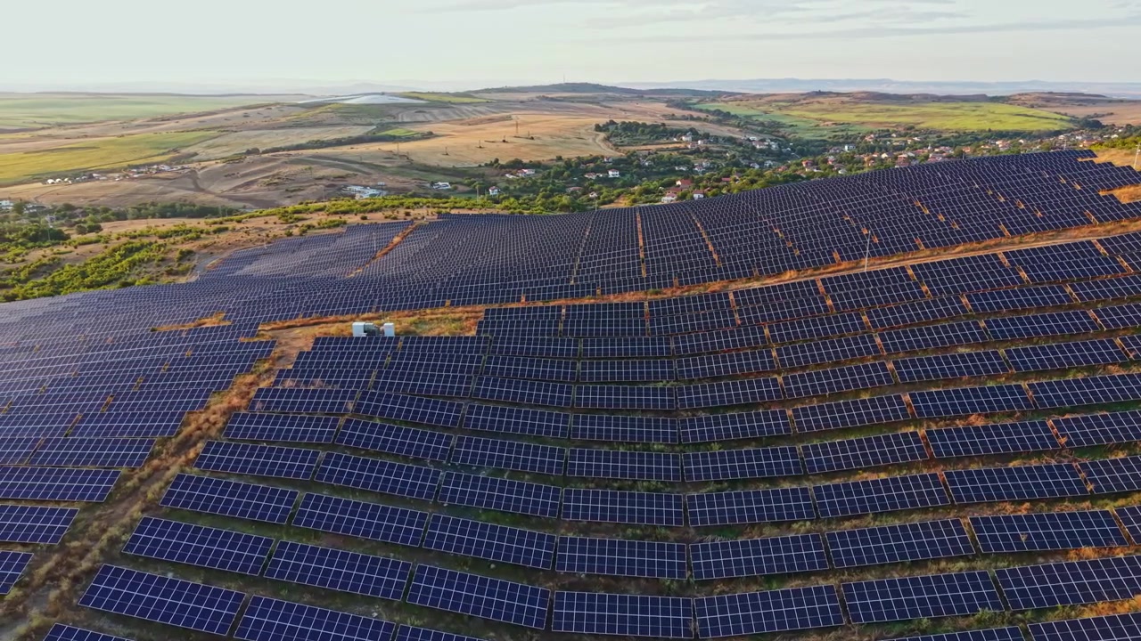 Stort solcelleanlæg på en bakkeskråning fanger sollys i et landområde om dagen