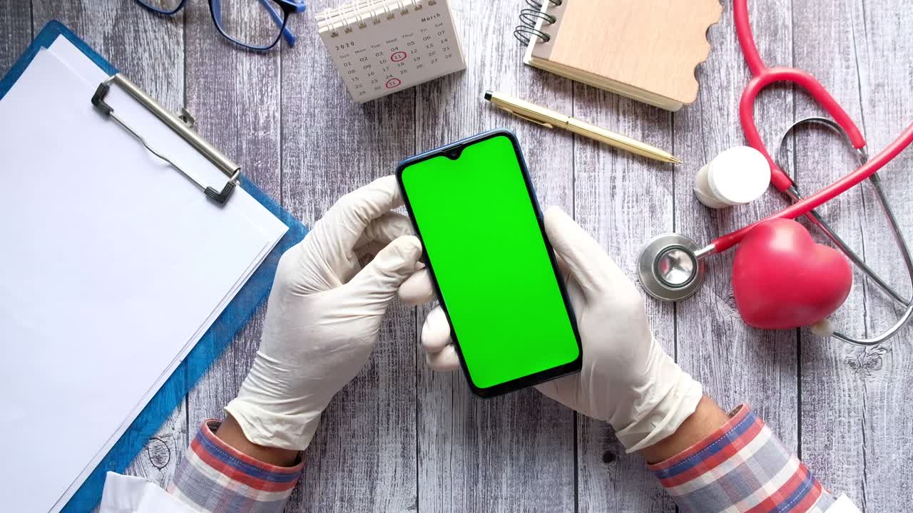 vista superior de la mano del médico en guantes de látex sosteniendo un teléfono inteligente con pantalla verde