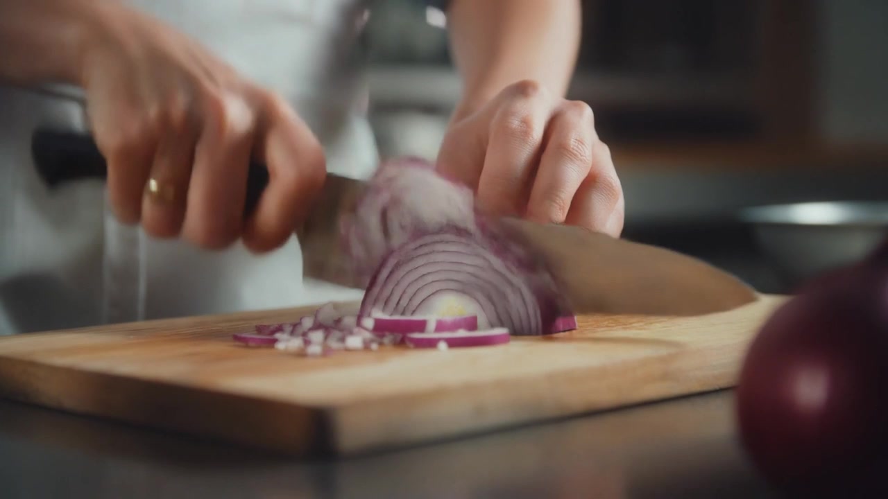 Chef che affetta una cipolla rossa su un tagliere di legno