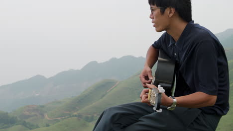 Stylish-handsome-man-concentrated-playing-the-guitar-on-top-of-a-hill-in-Southeast-Asia