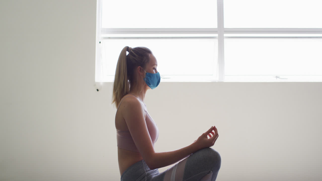mujer caucásica en forma con máscara practicando yoga en el estudio de yoga