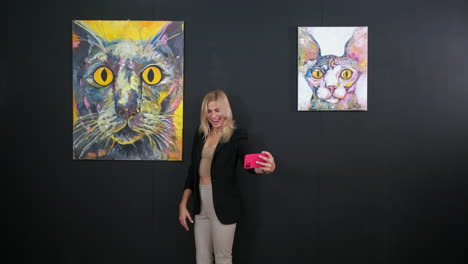 mujer tomando una selfie frente a pinturas de gatos en una galería de arte