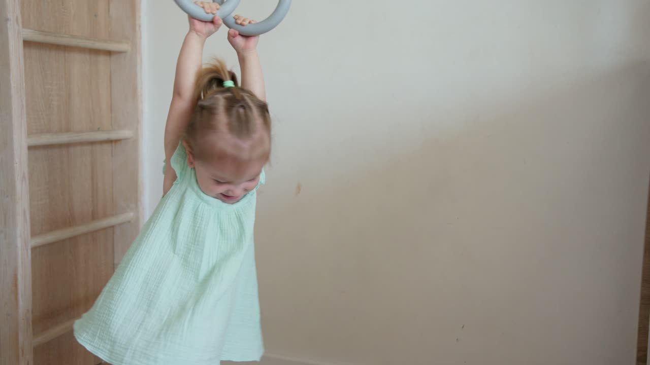 Happy Little Girl Playing on Gymnastic Rings Indoors