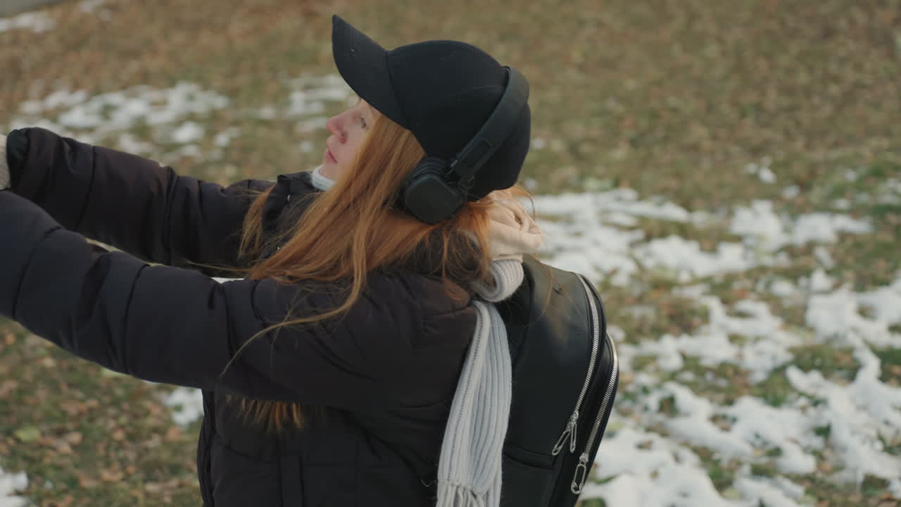Parkscene: Rødhåret kvinne henter et kosedyrkanin med hanskedde hender etter en hendelse med en snoker. Det er lette snøflekker på gresset, og hun har på seg ryggsekk, dunjakke og lue. Hun har utstrakte armer, et håpefullt smil og et naturlig uttrykk.