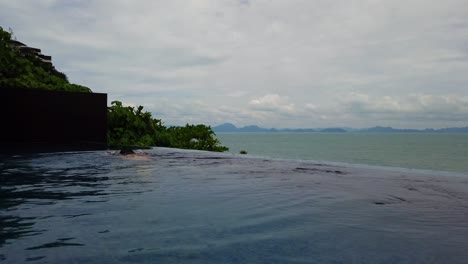asian man swimming at a infinity pool overlooking a beautiful ocean