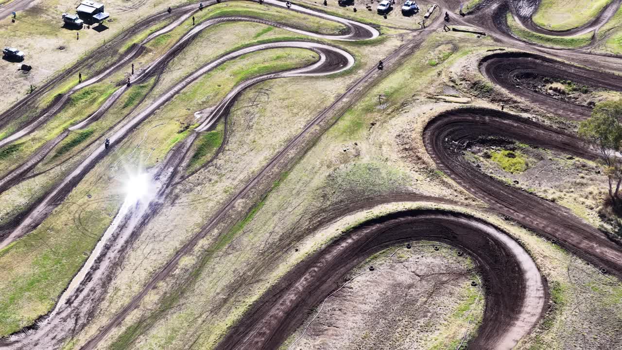 Drone captures motocross rider speeding along winding dirt track under bright daylight at moto park