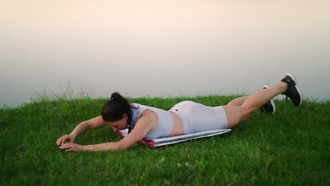 woman stretches her back and makes bends lying on the grass girl trains in the city park in nature.