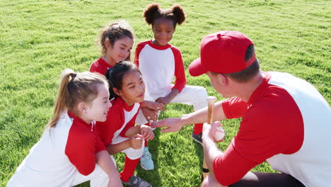 girls baseball team and male coach having team talk