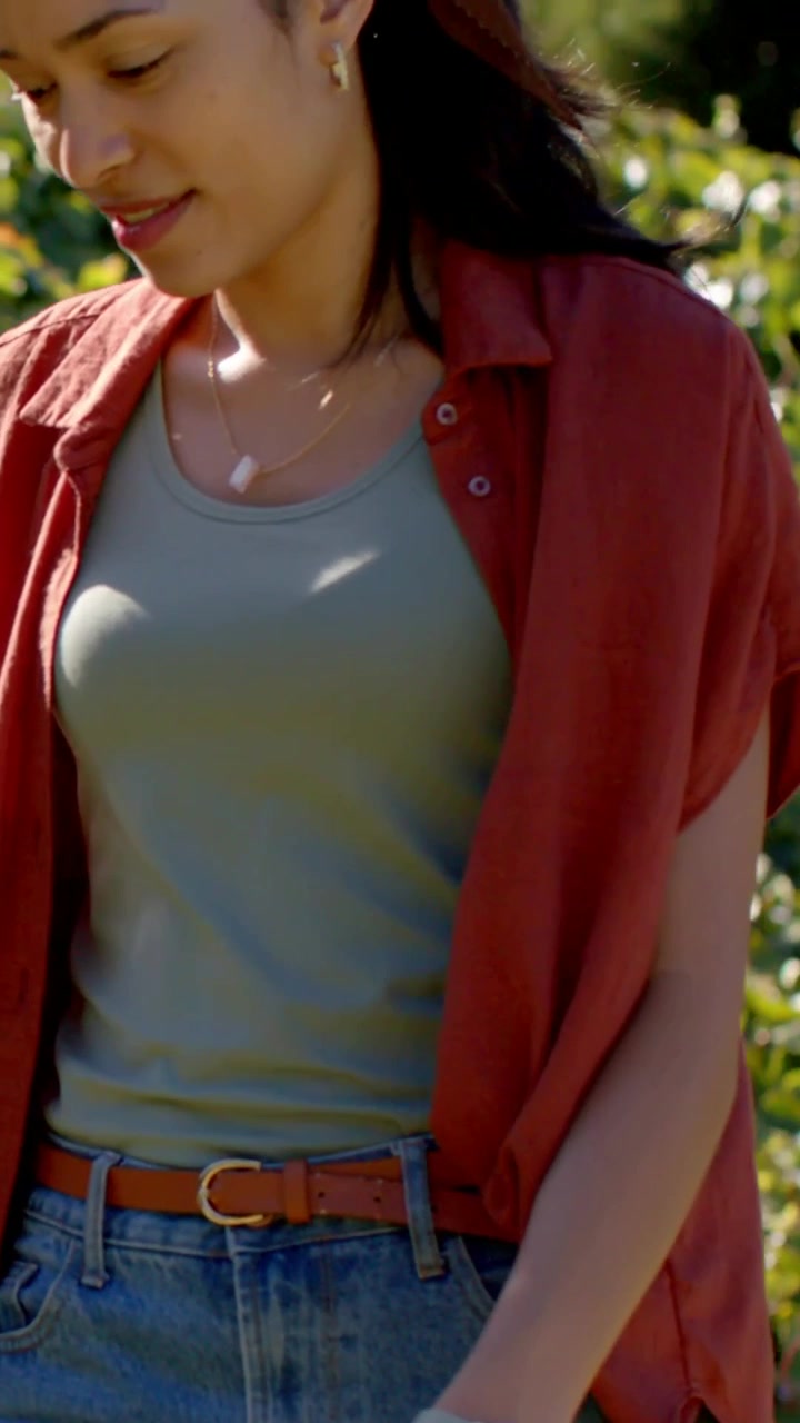 Video verticale: Donna che cammina in camicia color ruggine, canottiera e jeans, si muove attraverso un parco soleggiato mostrando l'orologio.