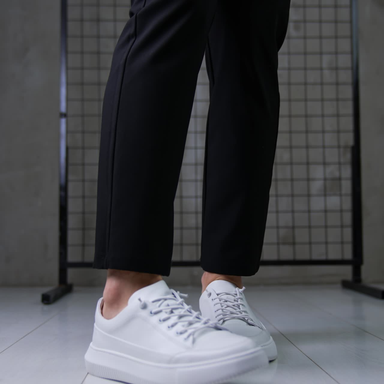 Woman wearing black trousers and white sneakers. Woman demonstrates her modern stylish look in grey studio. Close up