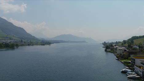 kussnacht flyover: moving over scenic water valley and village in alps mountains, switzerland, europe, drone | dramatic cinematic lowering shot of small homes on vast lake and countryside