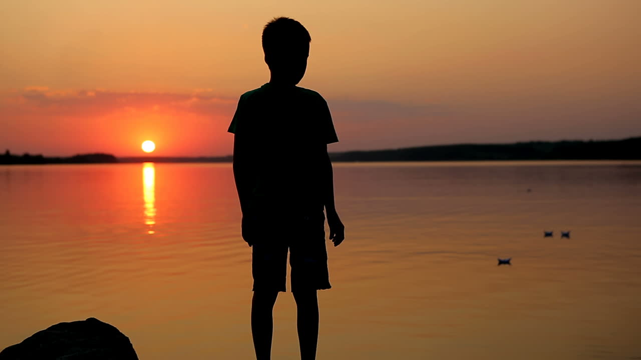 Boy With Paper Boat Near Water. Boy standing and holding paper boat on beach near water
