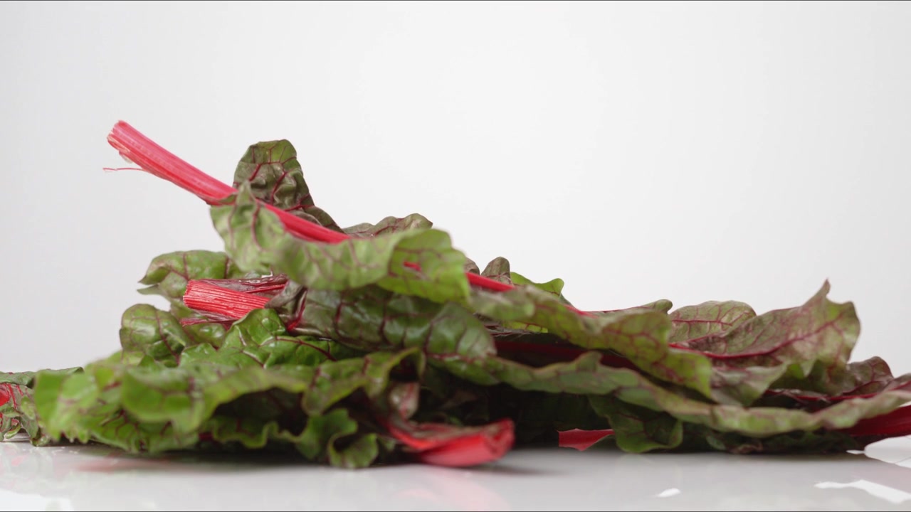 Fresh green Swiss Chard Leaves bouncing on a white tabletop in slow motion close up macro before settling.