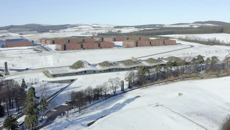 Vista-Aérea-De-La-Destilería-De-Whisky-Macallan-Rodeada-De-Nieve-En-Un-Soleado-Día-De-Invierno,-Moray,-Escocia---Tiro-De-Avance---Panorámica-De-Izquierda-A-Derecha