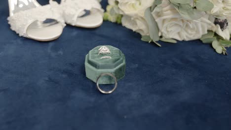 wedding ring on blue velvet display, white roses, heels, weddingday jewelry props, in out of focus, panoramic movement