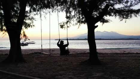 Silhouette-Eines-Mädchens,-Das-Am-Exotischen-Strand-Schaukelt-Und-Die-Schöne,-Ruhige-Lagune-Mit-Verankerten-Booten-In-Der-Dämmerung-In-Thailand-Beobachtet