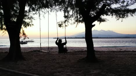 silueta de chica columpio playa exótica viendo hermosa laguna tranquila con barcos anclados al atardecer en tailandia