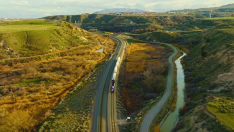 AERIAL---Train-on-railroad-tracks-among-mesas,-Bluffdale,-Utah,-circle-pan