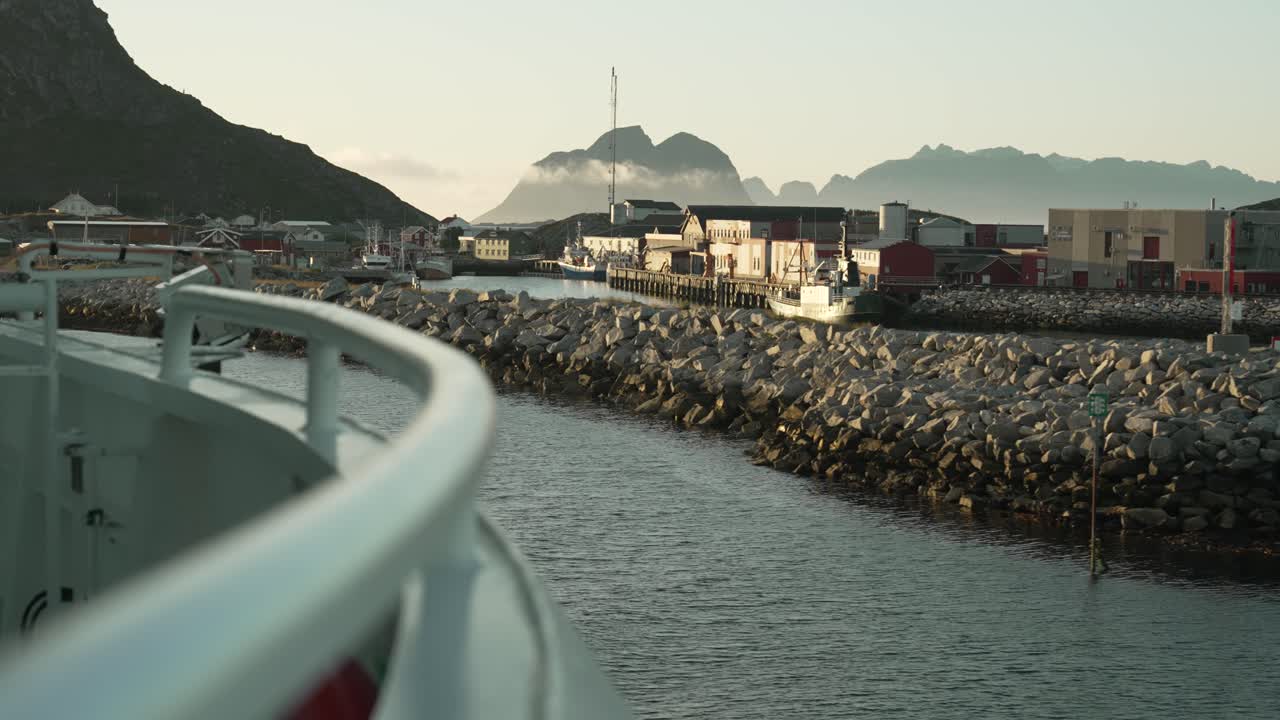 Watch a ferry depart from Værøy Island at sunset, with the island’s coastline slowly receding into the distance. Golden rays illuminate the calm sea and surrounding scenery