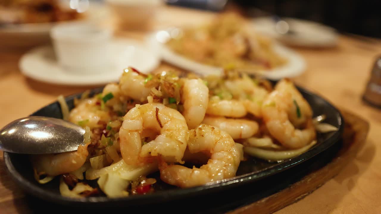 Close-up of steaming prawn stir-fry on hot plate, shallow focus, warm indoor lighting