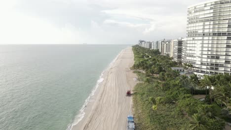 aerial follows sandboni as it cleans, rakes beach sand on miami beach