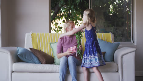 Front-view-Caucasian-girl-giving-flower-to-her-mother-at-home