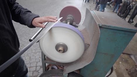 a man sharpening knives on a grinding wheel in the street