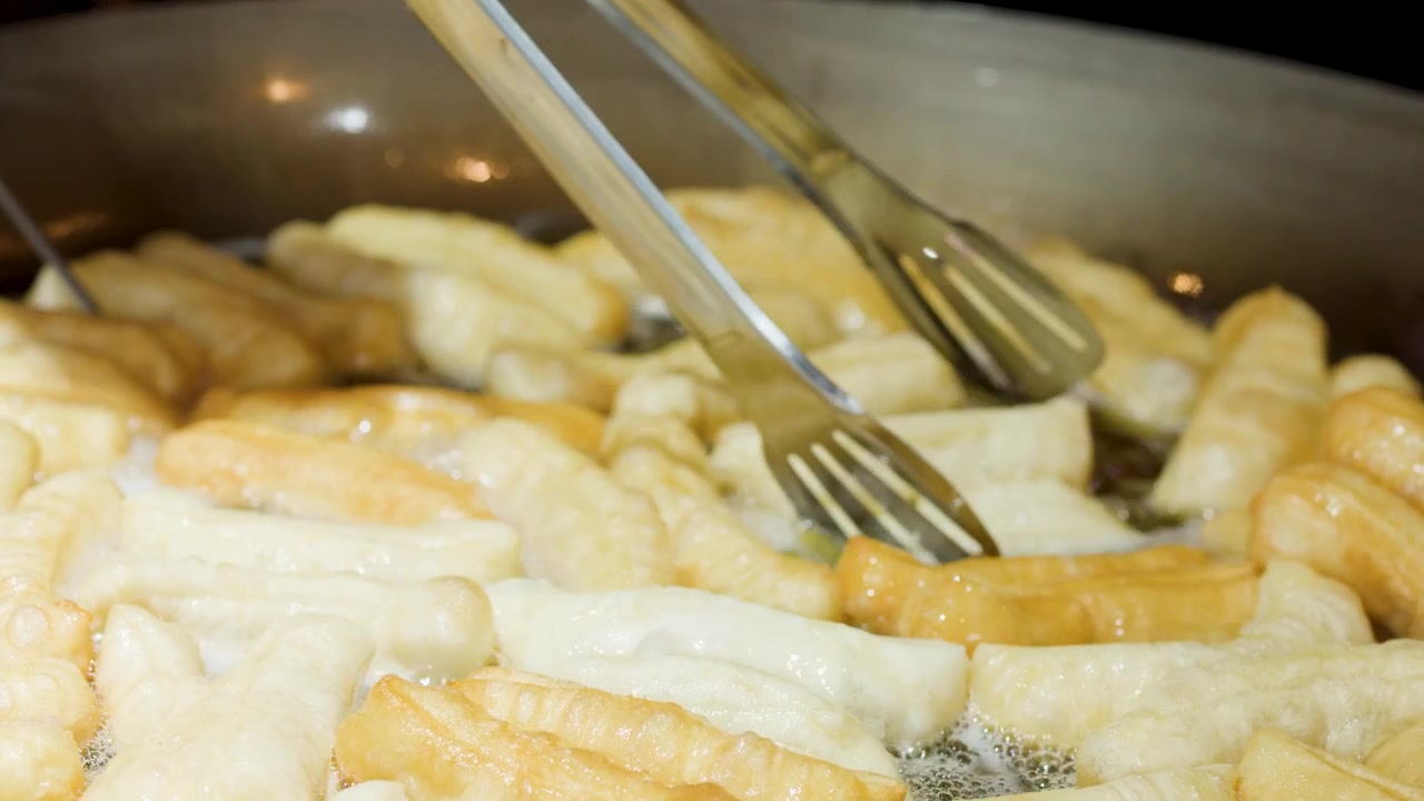 Friggere Youtiao (ciambelle cinesi) in olio bollente