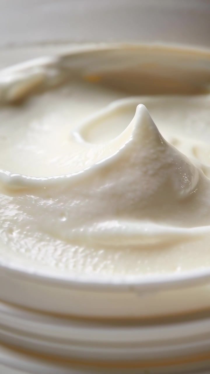 Video verticale: Spatola che tocca una superficie di crema chiara in un barattolo sul tavolo, formando una punta centrale