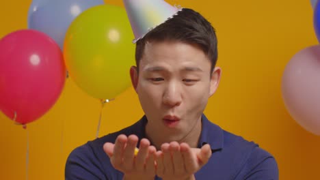 파티 모자를 입고 생일을 축하하는 남자의 스튜디오 초상화 카메라 1에 종이 콘페티를 불어넣는