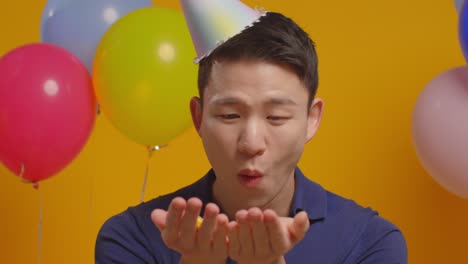 studio portrait of man wearing party hat celebrating birthday blowing paper confetti to camera 1