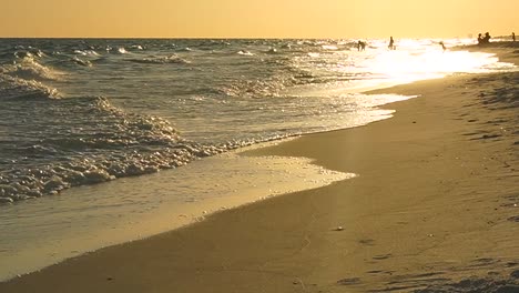 golden sun shines down on the last hour of the day and is reflected in slow motion waves as the run up the sand