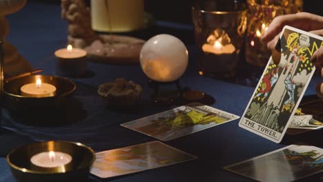 primer plano de una mujer dando lectura de cartas del tarot en una mesa a la luz de las velas sosteniendo la carta de la torre 1