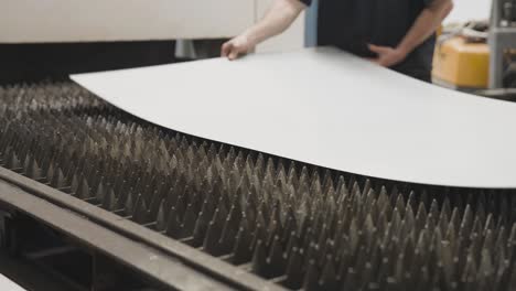 Workers-carefully-placing-sheet-of-metal-on-CNC-machine-platform,-industrial-workshop