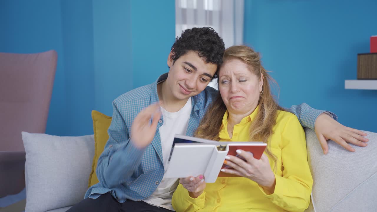 el joven y su madre están mirando el álbum de fotos juntos.