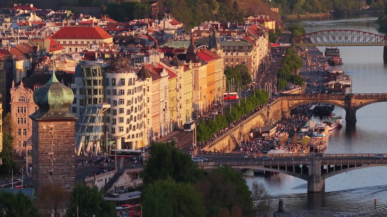 Vista aerea con drone del lungofiume della Moldava con più ponti, la Casa Danzante visibile a sinistra, colorate facciate storiche che fiancheggiano l'argine illuminate dalla luce del tramonto dell'ora d'oro, Praga