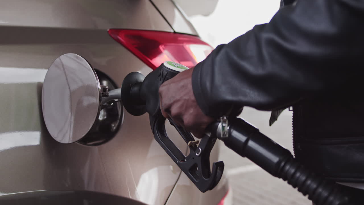 Primo piano di un uomo che fa rifornimento di benzina in auto presso una stazione di servizio, uomo afroamericano che fa rifornimento