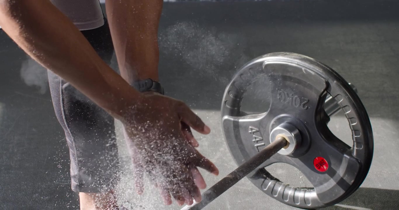 Rubbing chalk, mid-adult African man preparing for lift and gripping barbell 20KG on gym floor
