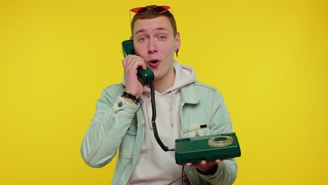 Cheerful-teen-man-secretary-talking-on-wired-vintage-telephone-of-80s,-says-hey-you-call-me-back