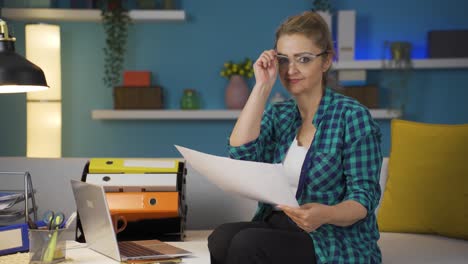 Home-office-worker-woman-smiling-at-camera-looking-at-paperwork.