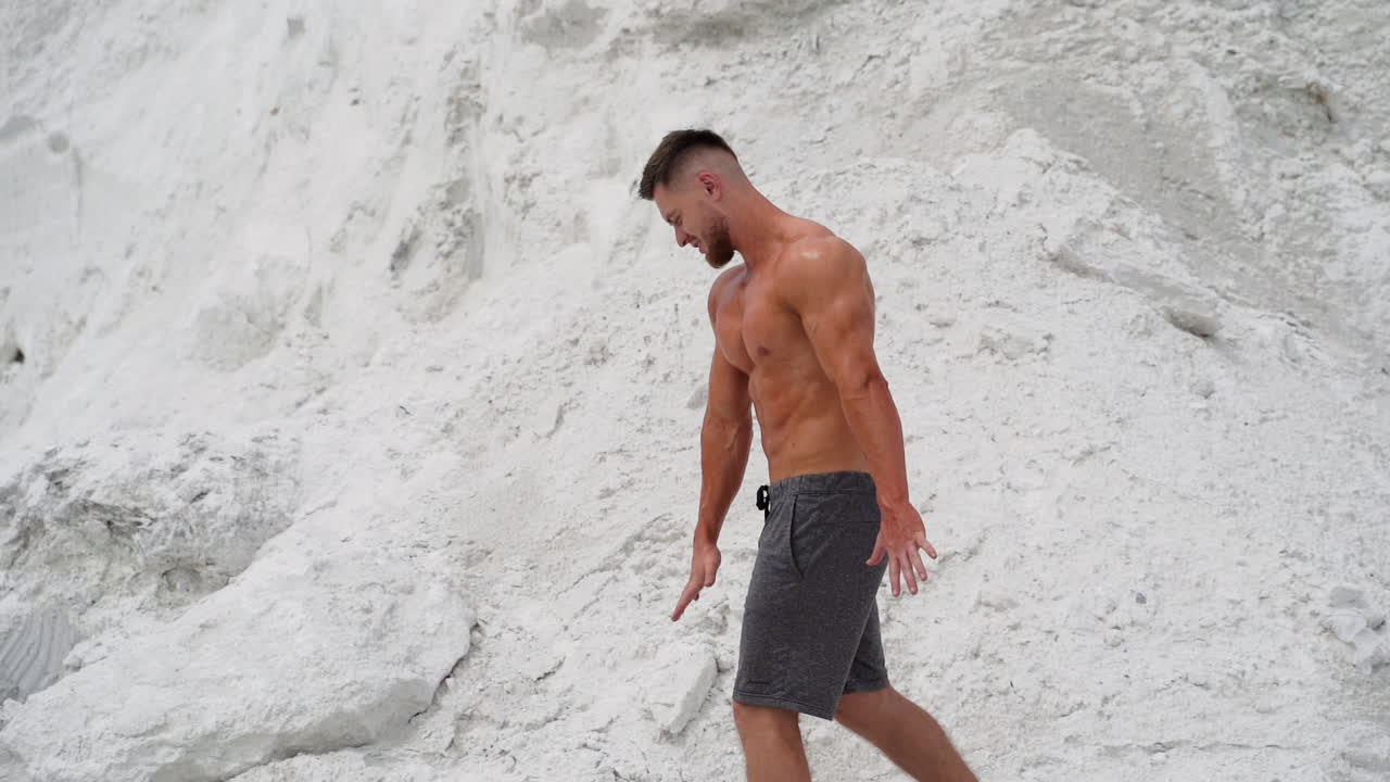 Shirtless bodybuilder in white mountains. Strong man turns back and shows his muscular body outdoors. Slow motion.