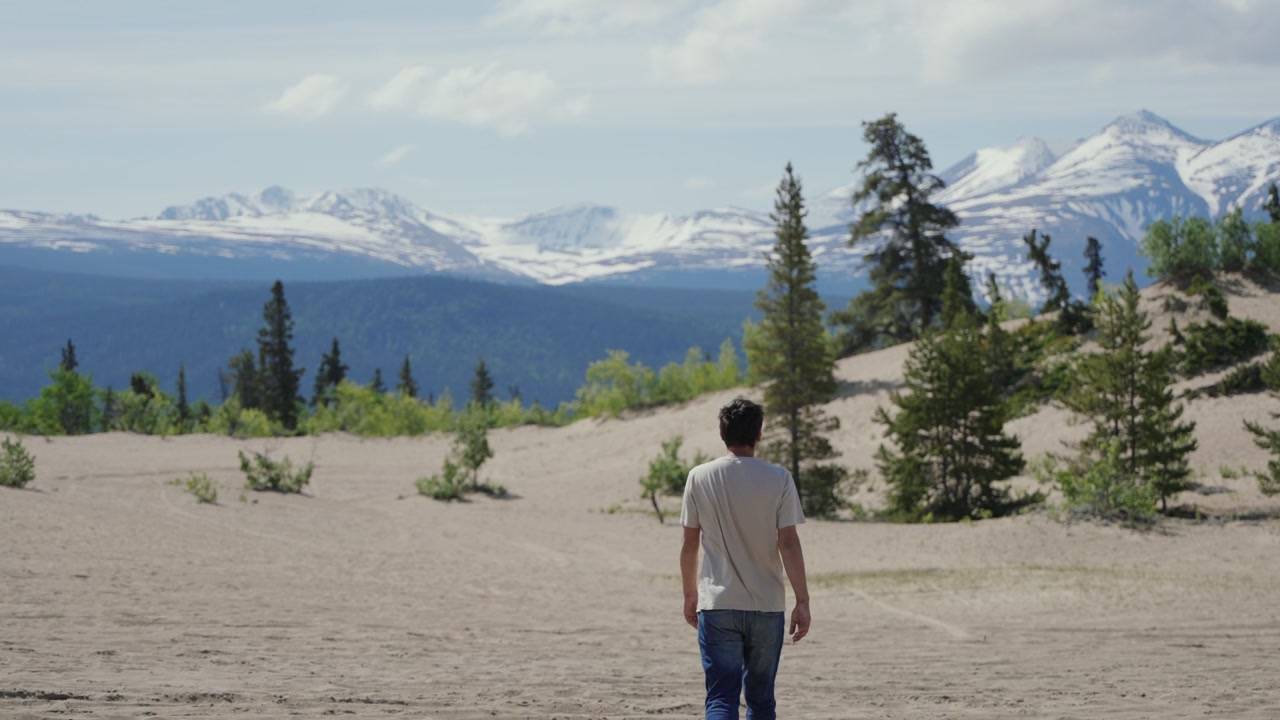 Man walking in Carcross desert looking at snow capped mountains in Yukon, Canada