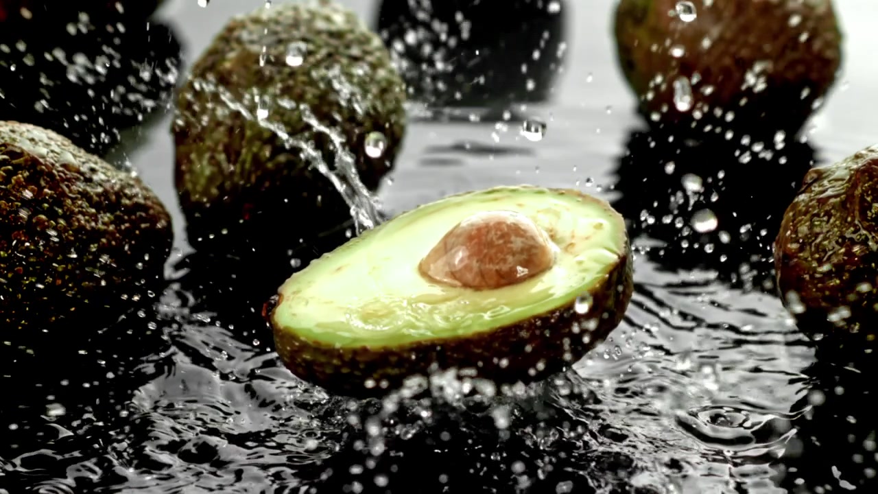 Avocado fresco dimezzato che schizza nell'acqua al rallentatore